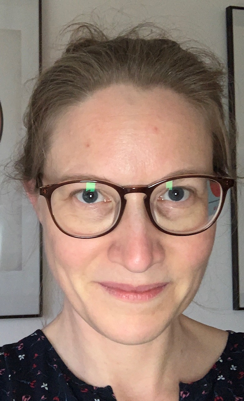 Frontalaufnahme von Claire Grauer, einer blonden Frau mit zusammengebundenen Haaren und Brille